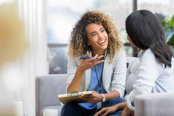 Stressed, Positive young female therapist gestures as she talks with a female client. The therapist smiles warmly as she talks with the young woman.